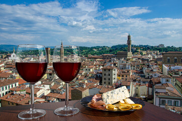 Two glasses of wine with cheese and meat snacks with view from above of Florence historic city center in Italy. Glass of red wine with different snacks - plate with ham, sliced, blue cheese.