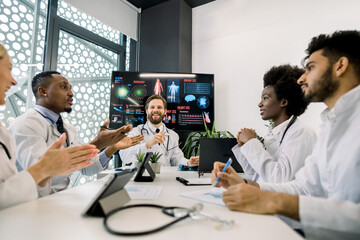 Multiracial team of doctors clapping their hands, applauding each other and enjoy successful meeting, discussing a patient case, using laptop, tablet computers. Close up view