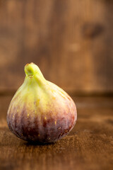 Close-up of a fig, on table and defocused wooden background, vertically, with copy space