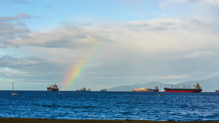 Obraz premium Shipping amongst nature' beauty, highlighted by rainbow, off BC coast. Viewed from Kitsilano Beach Park, Fall.