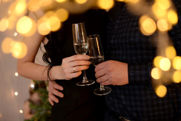 man and woman clink glasses of champagne against the background of a christmas tree