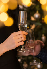 man and woman clink glasses of champagne against the background of a christmas tree