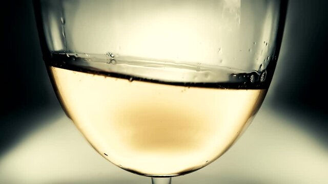 Creative macro slow motion video of white wine splashing in a glass from side to side like waves. Glass with splashing wine close-up. Old retro grunge vintage style.