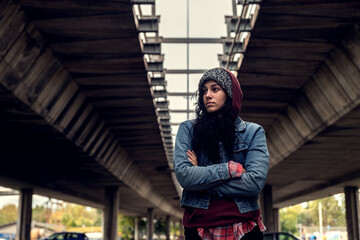 Young depressed homeless girl or woman standing alone under the bridge on the street on the cold...