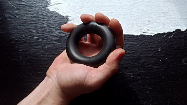 Man is training with the hand grip strengthener. Expander on the black background. Sporty wrist builder for everyday trainings.