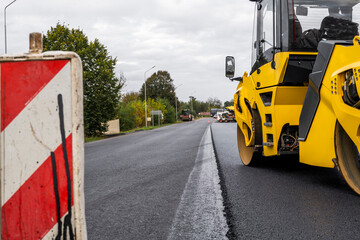 Asphalt road roller with heavy vibration roller compactor press new hot asphalt on the roadway on a road construction site. Heavy Vibration roller at asphalt pavement working. Repairing.