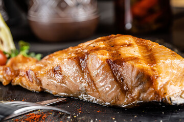 Grilled salmon red fish steak over an open fire. Serving food in a restaurant on black slate.