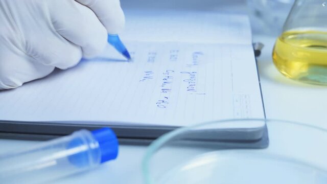 Food safety laboratory, scientist concept. Inspector writing test note on notebook after doing research in lab. Close up.
