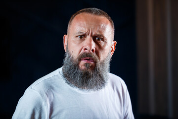 Obraz premium Emotional portrait of an adult gray-haired man with a beard in a white t-shirt