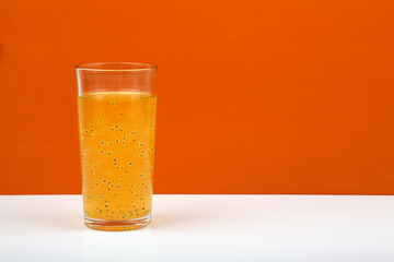 A glass of fruit orange juice with passion fruit seeds on white table against orange wall