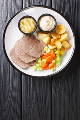 Tafelspitz is boiled beef in broth, served with a vegetables and horseradish close-up in a plate on the table. vertical top view from above