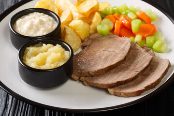 classic Austrian main dish Tafelspitz is beef simmered until tender then served with a variety of vegetables and horseradish sauce close-up in a plate on the table. horizontal