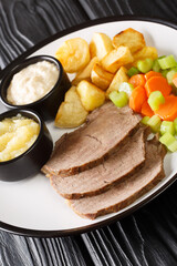 Typical Austrian Tafelspitz cooked with good beef, fresh vegetables, aromatic seasoning served with potatoes, horseradish and apple sauce close-up in a plate on the table. vertical