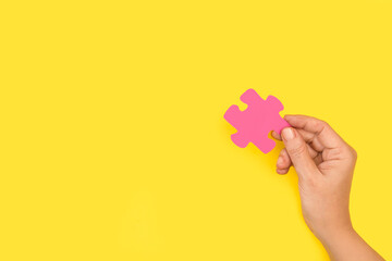 Mano sosteniendo una pieza de puzzle rosa sobre un fondo amarillo liso y aislado. Vista de frente....