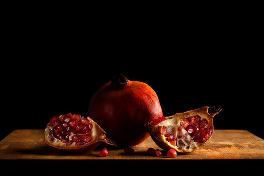 Baroque style still life with a whole pomegranate and two quarters on a wood and dark background.