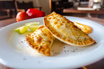Jamaican Patties usually tinted in golden or yellow colors, mounted on a plate with tomato, lettuce, cucumber, lemon and mustard.