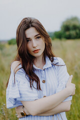 attractive woman dressed in a long shirt posing for a photo in a field among weeds and wildflowers