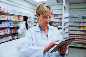 Caucasian female pharmacist scrolling on digital tablet standing concentrating in pharmacy 