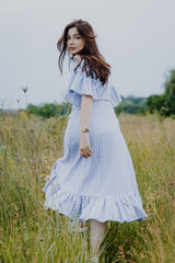 Fototapeta na wymiar attractive woman dressed in a long shirt posing for a photo in a field among weeds and wildflowers