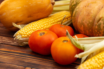 Pumpkin, corn and tomatoes on brown wooden background