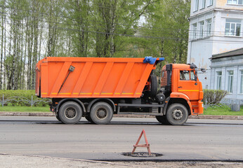 Road equipment on the street of the city in Russia. Russian truck 'Kamaz' dump truck orange with body and cabin, with three axles. Repair work on the road in the spring