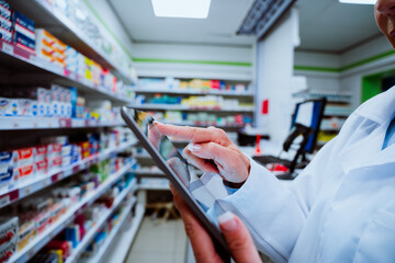 Close up of pharmacist checking medication on digital tablet walking through isles in pharmacy drugstore