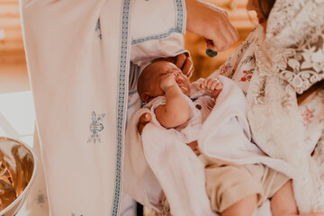 rite of sacrament of epiphany child baby in church. priest blesses child, smears with holy water,...