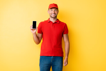 delivery man in red cap holding smartphone with blank screen on yellow