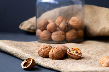 walnuts. unpeeled and peeled walnuts in shells on a black table and in a glass jar. brown nuts with sackcloth on a dark background. copy space. dried walnut and fruit.
