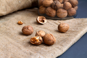 close-up three walnuts. unpeeled and peeled walnuts in shells on a black table and in a glass jar. brown nuts with sackcloth on a dark background. copy space. dried walnut and fruit.