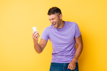 happy man holding smartphone and laughing on yellow