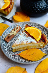 An vertical view of a slice of delicious lemon pie on a serving plate with cinnamon sticks and autumn yellow leaves. Homemade cakes closeup.