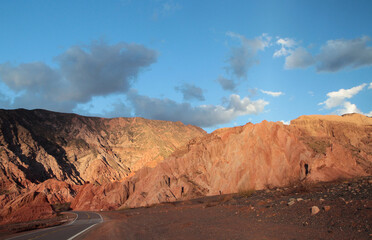 The asphalt highway across the desert at sunset. Beautiful panorama view of the empty road along the arid valley, the red sand, sandstone and rocky hills with a dusk light.