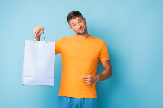 Confused Man In T-shirt Pointing With Finger Shopping Bag On Blue