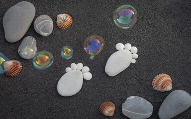 Arrière-plan grains de sable de mer, sable fin noir de plage. Bulles de savon. Galets en forme de petit pied pour annoncer une naissance.	