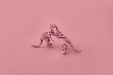 Toy models of dinosaur skeletons on a pink background.