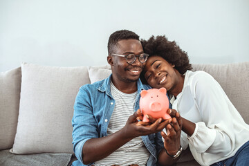 Portrait of a black couple holding their savings in a piggybank and looking very happy. Multiracial...