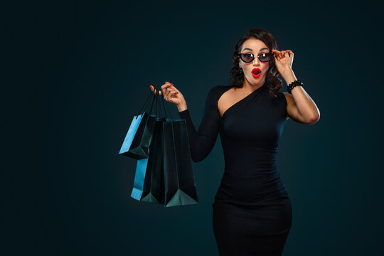 Black Friday sale concept for shop. Girl in sunglasses holding big bag isolated on dark background at shopping on blackfriday.