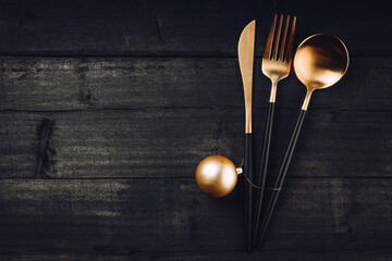 Golden cutlery and christmas ball on black wooden background, concept of new year table setting in...