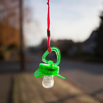 A green plastic baby pacifier dangling from an orange lanyard