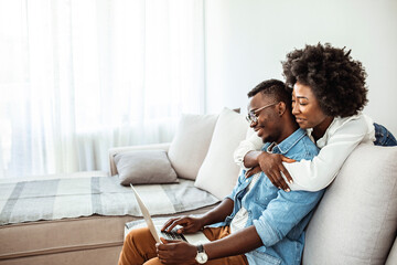 Naklejka na ściany i meble Happy African American couple using laptop, receive good news online, email, positive decision from bank, smiling wife and husband looking at screen together, mortgage or loan approve paper letter