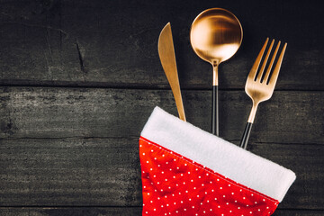  Golden cutlery in santa hat on black wooden background, concept of new year table setting