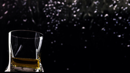 A glass of whiskey on a black background with drops. Close-up of a glass of whiskey, brandy or...