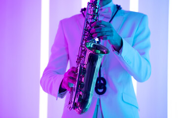 Man's hands with saxophone against the background of neon lamps. Fingers playing a saxophone. Close...