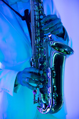 Fototapeta premium Partial view of stylish professional musician in white suit playing saxophone. Hands and musical instrument close up.