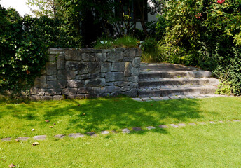 Old stone steps in the park. Lawn and trees. Landscaping. Support wall.