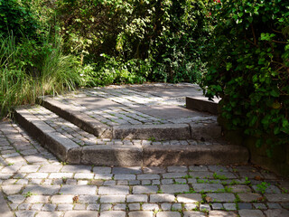 Old stone steps in the park. Lawn and trees. Landscaping. Support wall.