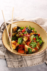 Oriental cuisine. Mr. Chaw's salad. Salad from fried eggplant, tomatoes, cucumbers, chili peppers, onions and fresh herbs with chopsticks in a beige plate on a grey table. Background image, copy space