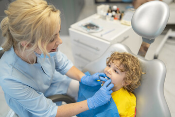 Cute young boy visiting dentist, having his teeth checked by female dentist in dental office.