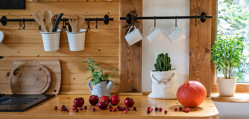 Vintage rustic kitchen in a cottage with wooden wall and counter with cranberry. Kitchenware with cup and mug in cozy interior with window and plant. Banner